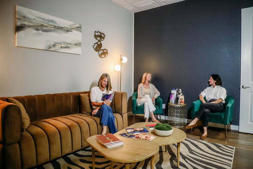 Clients relaxing and chatting in the modern waiting area of a medical aesthetics clinic with warm, inviting décor.